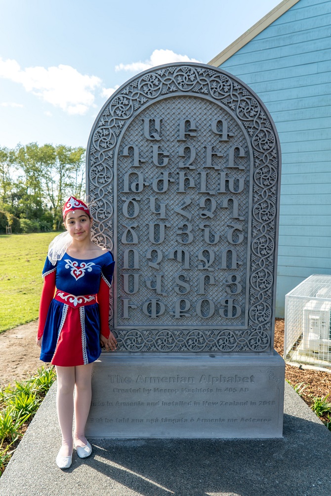 Taisia Grigoryan, stands next to the Armenian Alphabet Monument. The alphabet was carved in Armenia and shipped to New Zealand in 2018. (Photo: Tamara Azizian)
